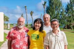 Collaborating entomologists pose in front of coconut trees damaged by the invasive coconut rhinoceros beetle