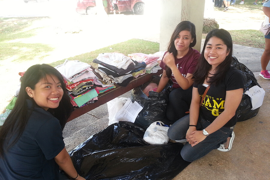 Students Hermi-Alyss Schacher, Vanessa Tudela, and Leizl Llegado distribute clothing 