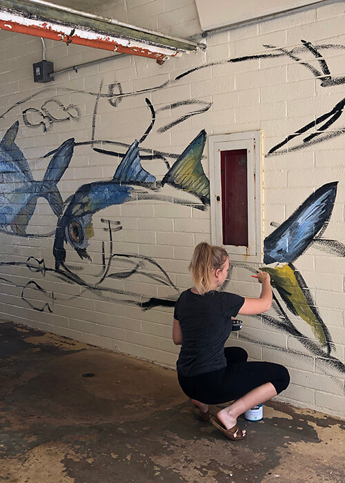Marine biology major Constance Sartor paints a large jack on a Marine Lab wall