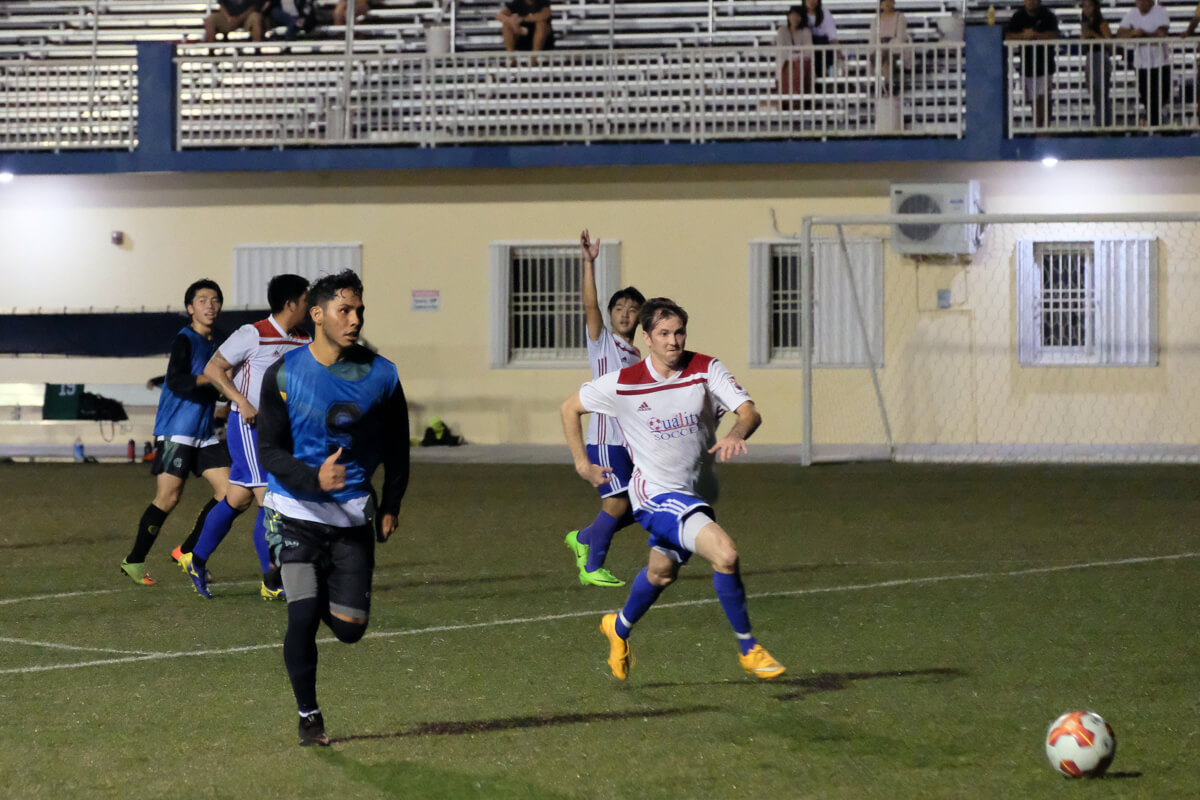 Hezekiah Cruz looks to pass the ball downfield against an oncoming Quality Distributors defender