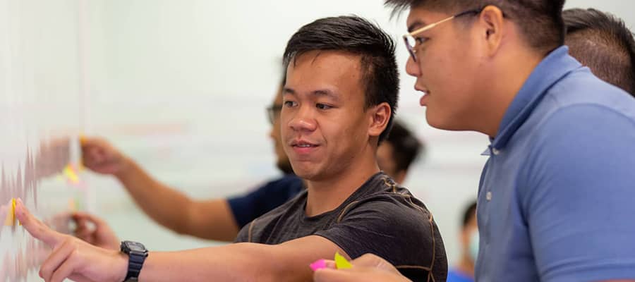 A photo of two male students discussing in front of a white board