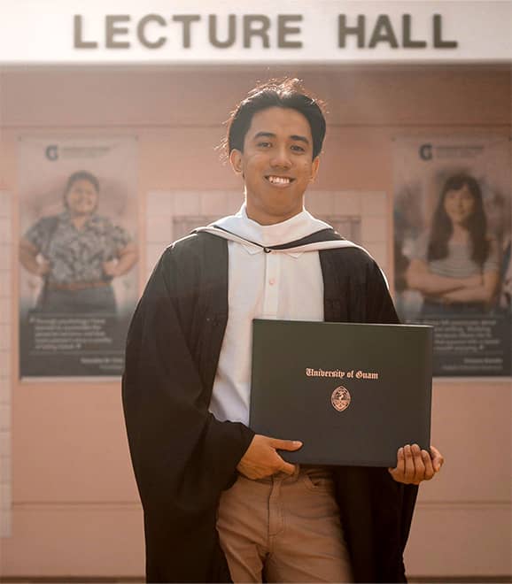 UOG student poses in front of Lecture Hall with Bachelor’s Degree