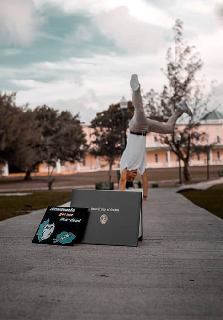 UOG student does handstand behind Bachelor’s degree sitting on ground