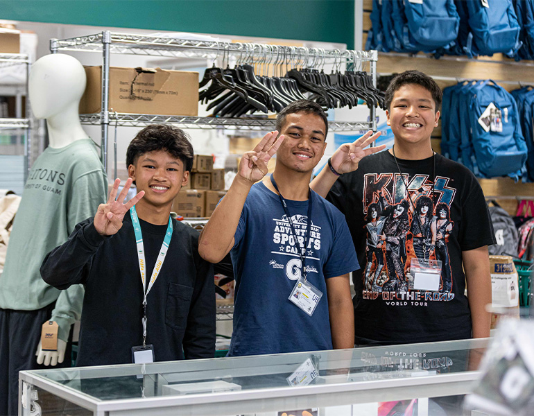 Three young interns pose for a photo in the Triton Store holding up the Triton hand sign