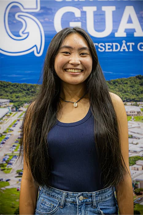 Student poses for photo at UOG New Student Orientation in front of UOG poster