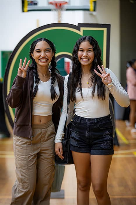 Two students pose for photo at UOG New Student Orientation in front of Triton G sign