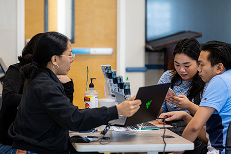 Photo of two staff from the UOG Office of Information Technology assisting two students.