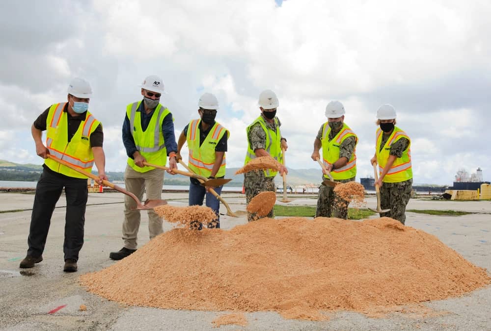 6 men wearing construction hats and vests dig at the ground with shovels for NAVFAC ceremony