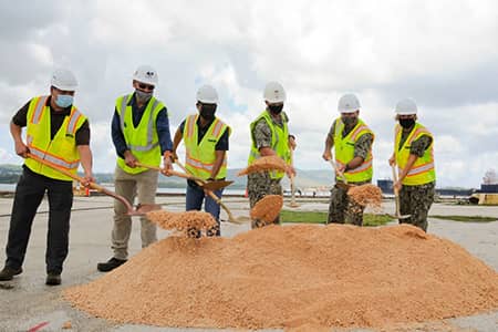 6 men wearing construction hats and vests dig at the ground with shovels for NAVFAC ceremony