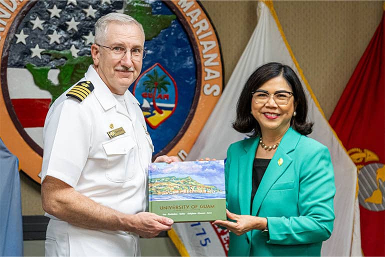 Anita B. Enriquez and Cap. Brown both hold coffee table book about UOG at NAVFAC Marianas.