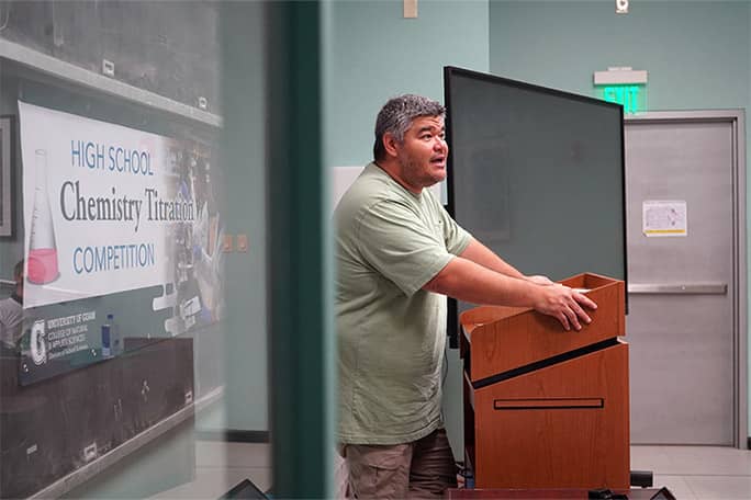 Dr. John Limtiaco speaks at podium for UOG Chemistry Titration Competition