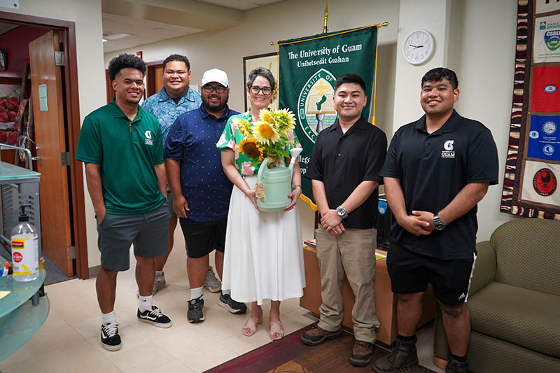 A group of students presenting a vase of sunflowers to a university administrator.