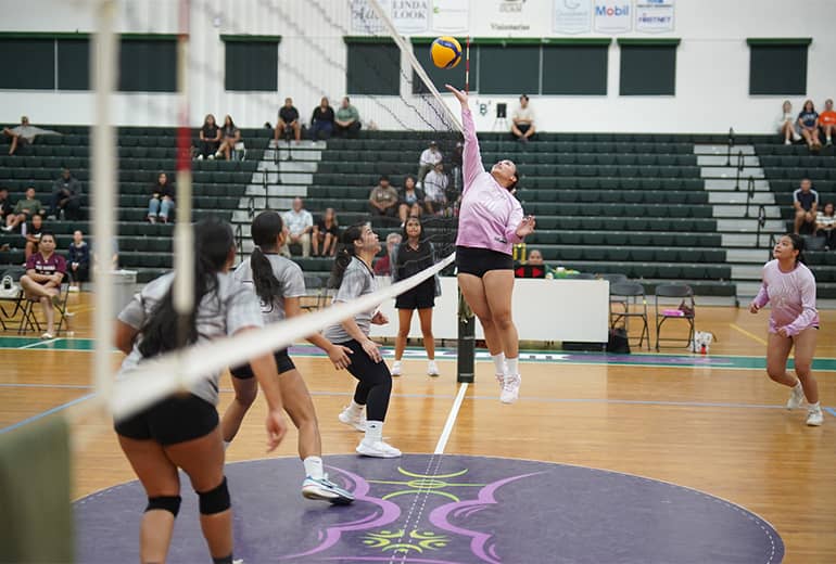 Lady Triton spikes ball over net while opponents try to block