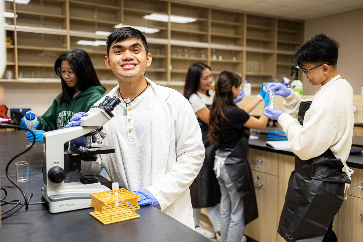 Photo of a UOG student posing next to a microscope