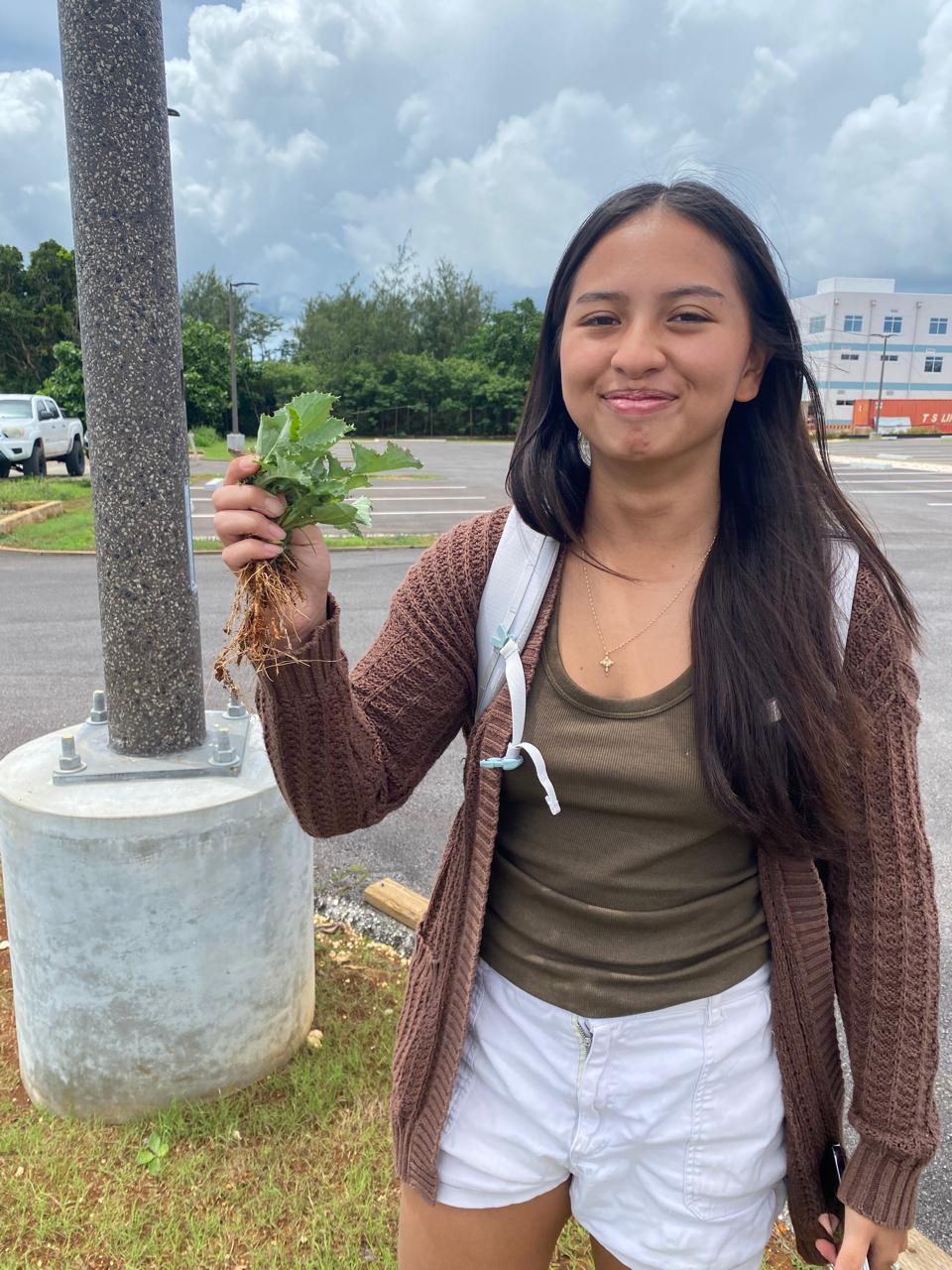 Biology major Samaria Quinata holds a common sowthistle she uprooted on campus in October as part of her Plant Biology class’s continued efforts to remove the weed from campus and keep it from spreading. A woman holding an uprooted weed