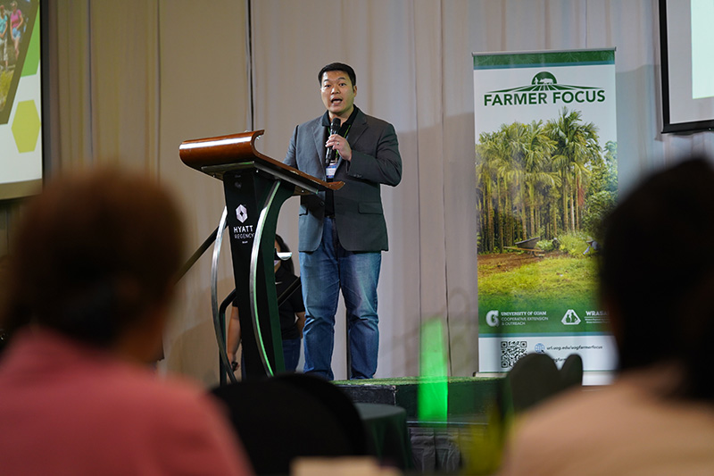 A man speaking into a mic on stage with a Farmer Focus banner in the background