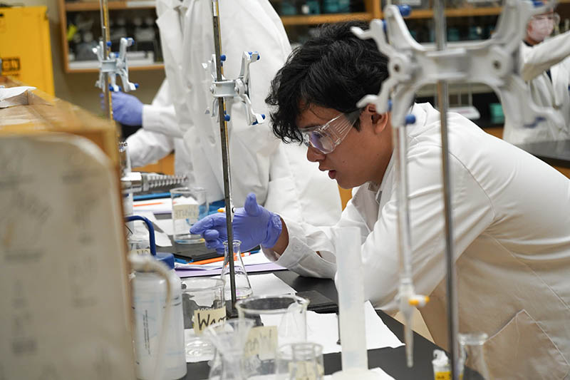 A high school student in a lab coat working with liquids in the lab