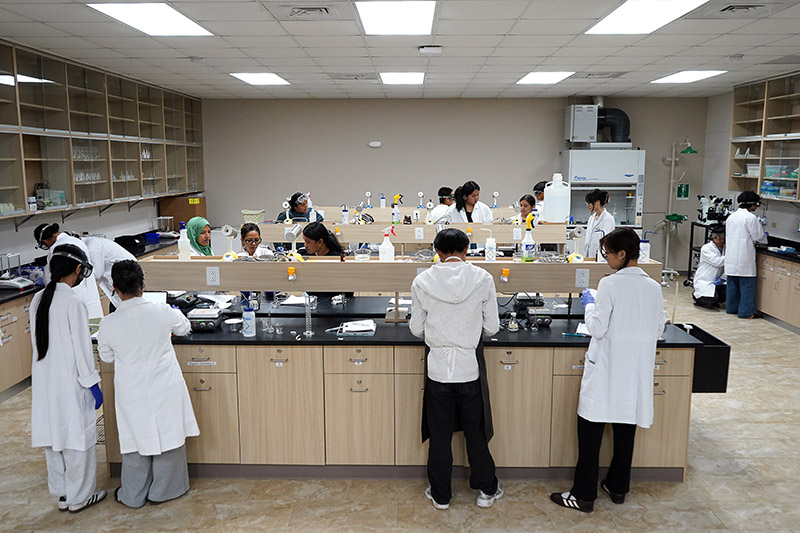 A wide-angle view of a chemistry lab showing many students in lab coats working at different stations.