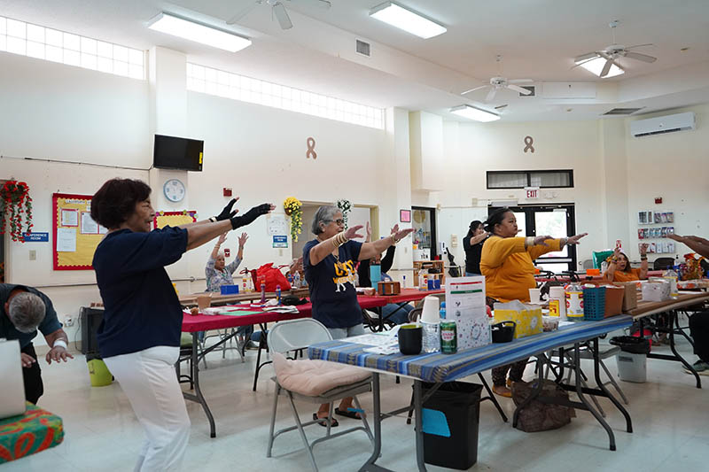 A room of older adults standing with arms in the air doing exercises