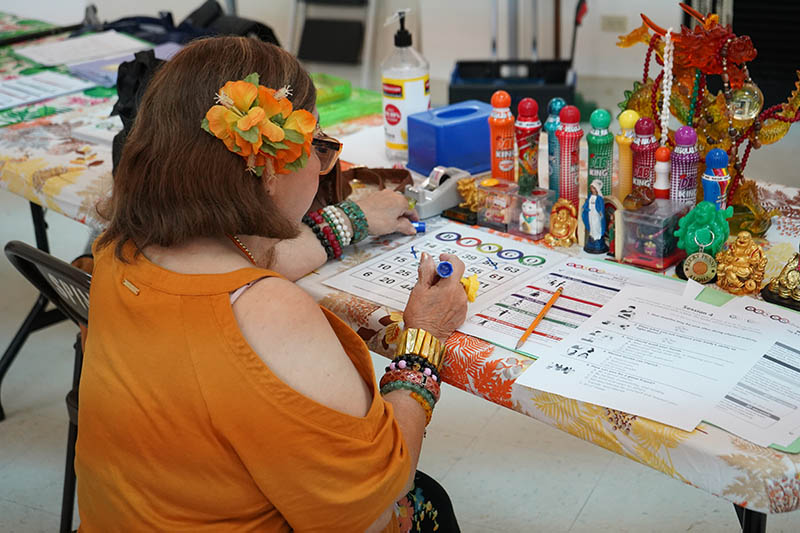 A woman sitting at a table marking Bingo cards and surrounded by good luck charms